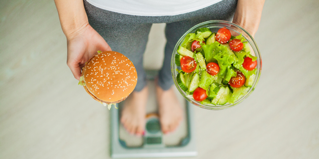 Une femme se tenant sur une balance compare un hamburger et une salade